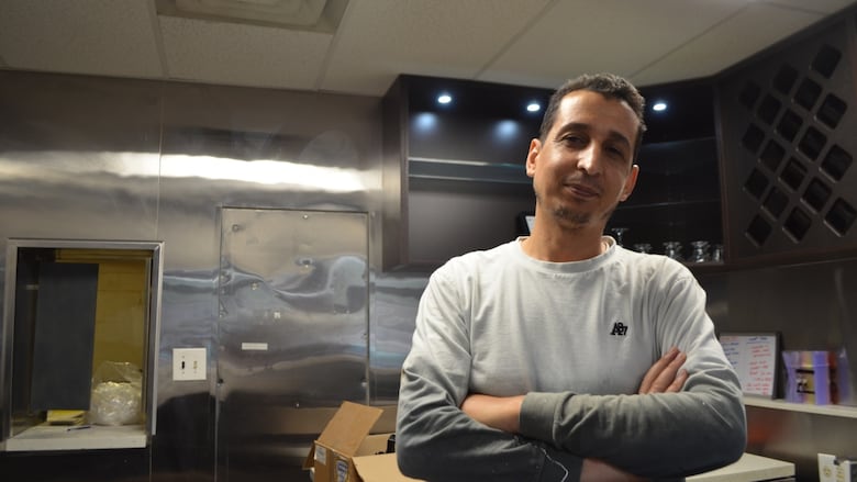 A person poses with their arms crossed in a kitchen