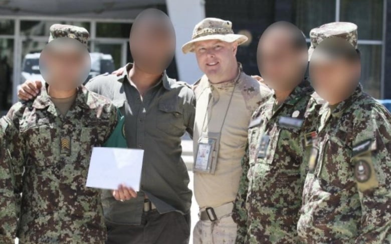 Five men in military uniforms stand next to each other. Some of their faces are blurred out.