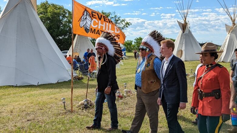 Edwin Ananas, David Pratt and Marc Miller walk in a row with a orange "every child matters" flag blowing beside them.