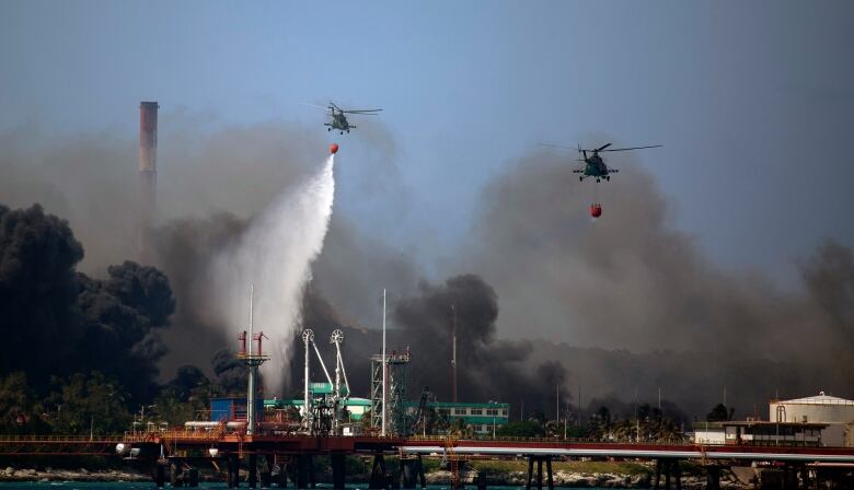 Two helicopters flying over black smoke rising from an industrial facility.