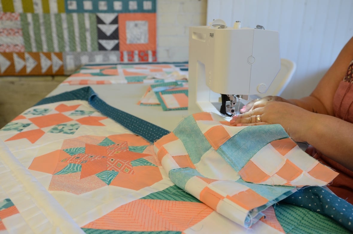 A close up of hands sewing a quilt together with a machine. 