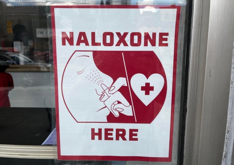 تابلویی در پنجره می گوید Naloxone اینجا و تصویری از اسپری بینی دارد. 