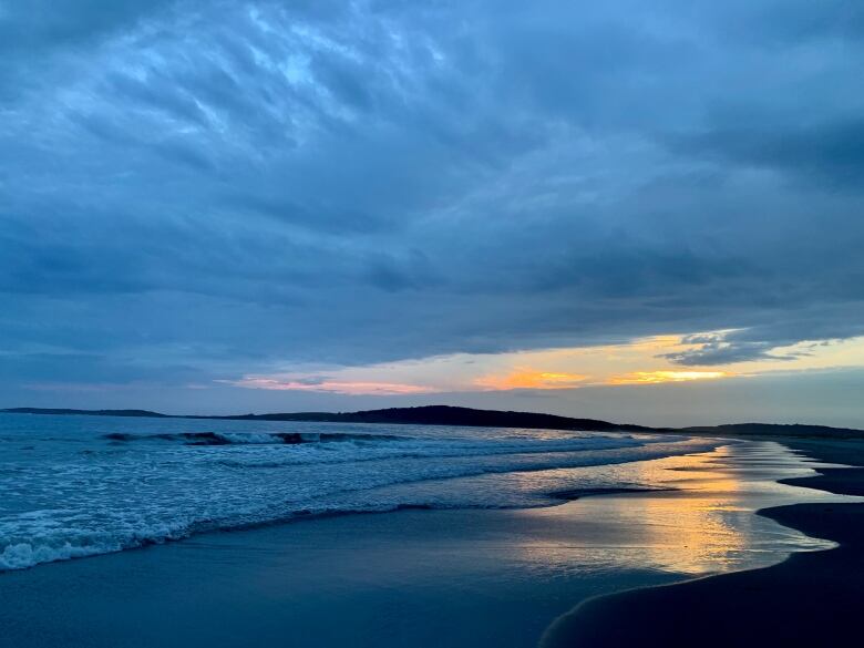 The sun sets on a sandy beach.