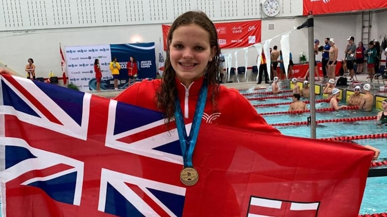 A teenager wearing red has a gold medal around her neck, as she holds up the Ontario flag.