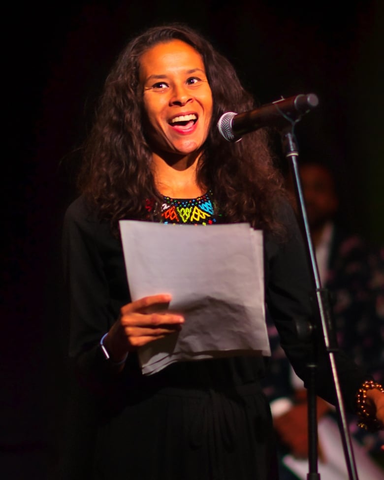 Black woman with long hair speaking at a podium with her notes in her hand