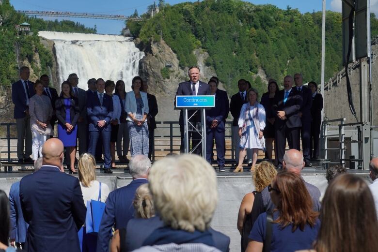 Legault standing in front of party candidates with a huge waterfall in the backdrop.