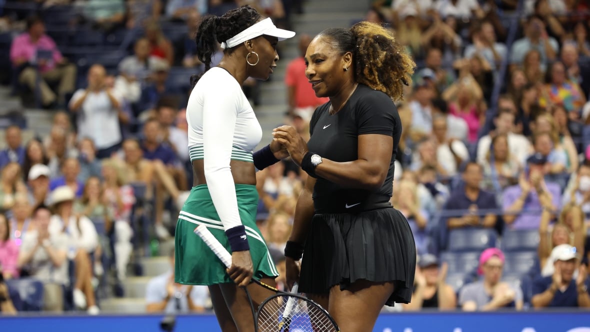 Sisters Serena Williams, right, and Venus Williams of the United States clasp hands on a tennis court.