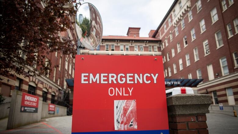 A red sign reading 'EMERGENCY ONLY' is in front of a hospital.