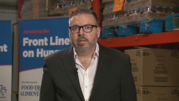 Stephane Sirois, executive director of the Food Depot Alimentaire, said this funding was a long time coming. A man with black glasses wearing a black suit jacket. He is standing in a warehouse.