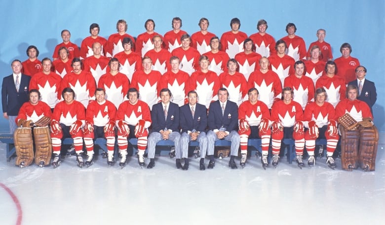Players and coaches lined up "class photo" style, with the coaches sitting front row centre. Players wear red and white uniforms while coaches wear blue blazers and grey slacks.