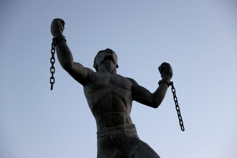 A statue of a man with broken chains in each hand.