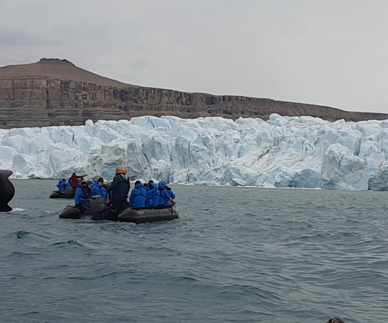 Small boats float in front of an ice wall on an island