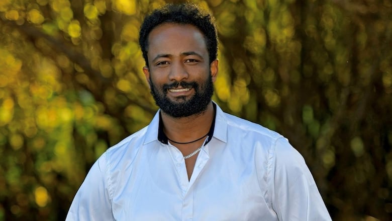 A man stands against a background of trees and smiles for the camera.
