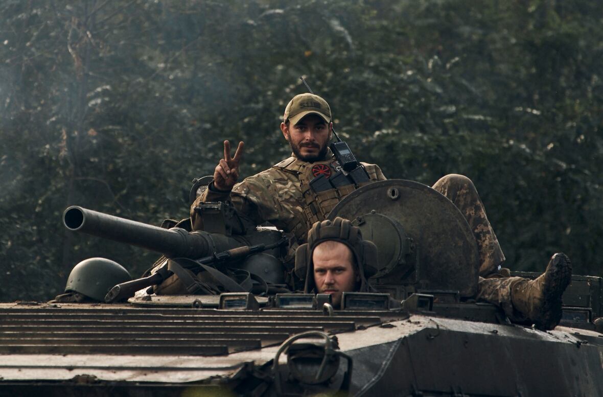 Soldiers atop a tank, with one giving the peace sign.