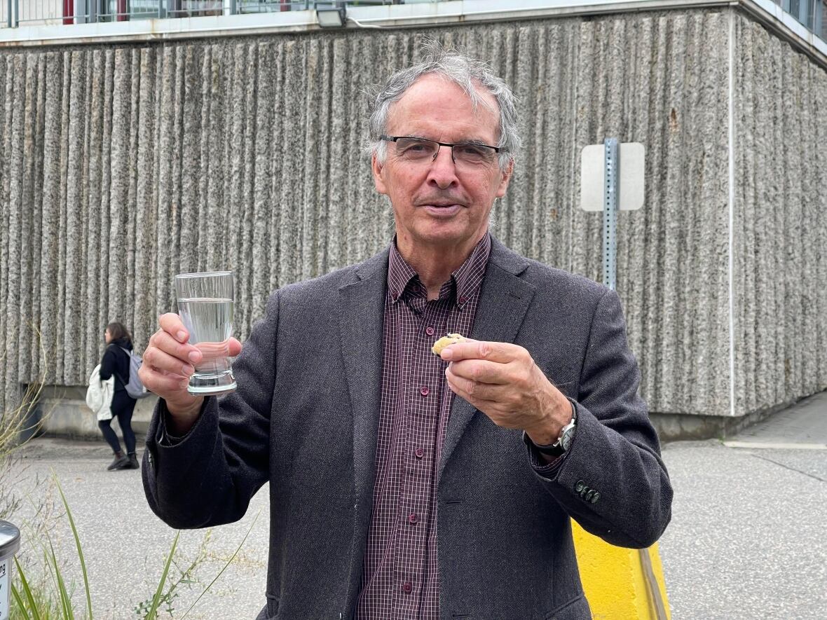 A man holding a glass of water and a muffin.