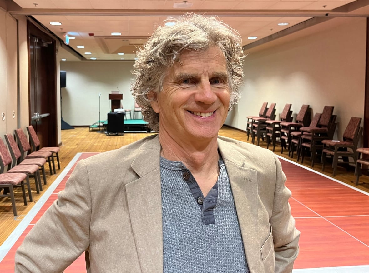 A man stands smiling in a hotel ballroom.