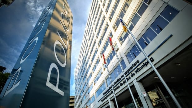 A low-angle shot shows a tall vertical sign reading "police," in front of a large office building with a "Winnipeg Police Service Headquarters" sign on its front.