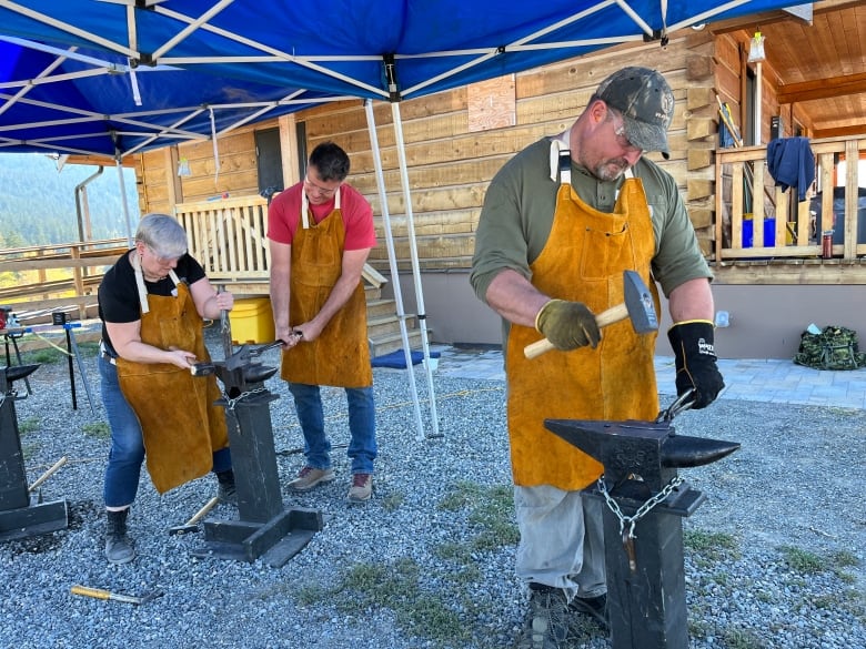 A group of people stand over anvils, with metal instruments.