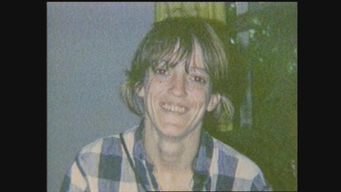 A woman with dark hair in a plaid shirt smiles at the camera in a decades-old photograph.