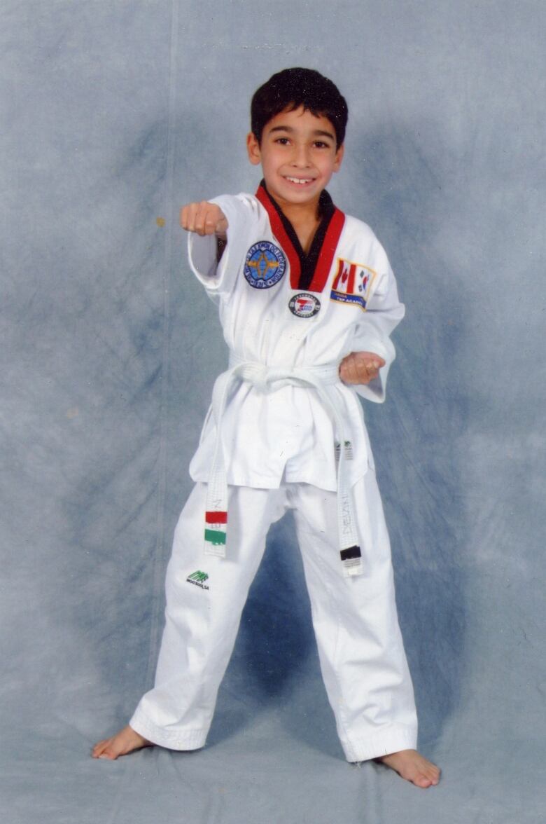 A young boy wearing white taekwondo uniform stands facing straight ahead.