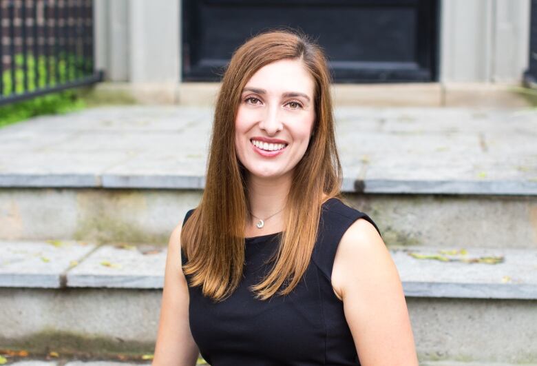 A smiling woman sits for a photo on a set of steps outside a building. 