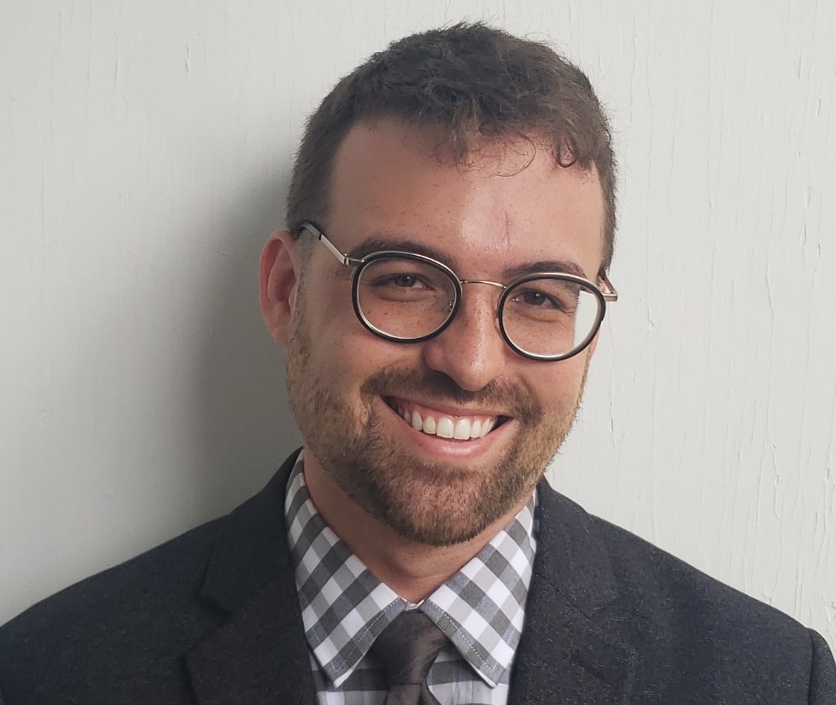 A man with short brown hair and glasses in a suit and checkered shirt.