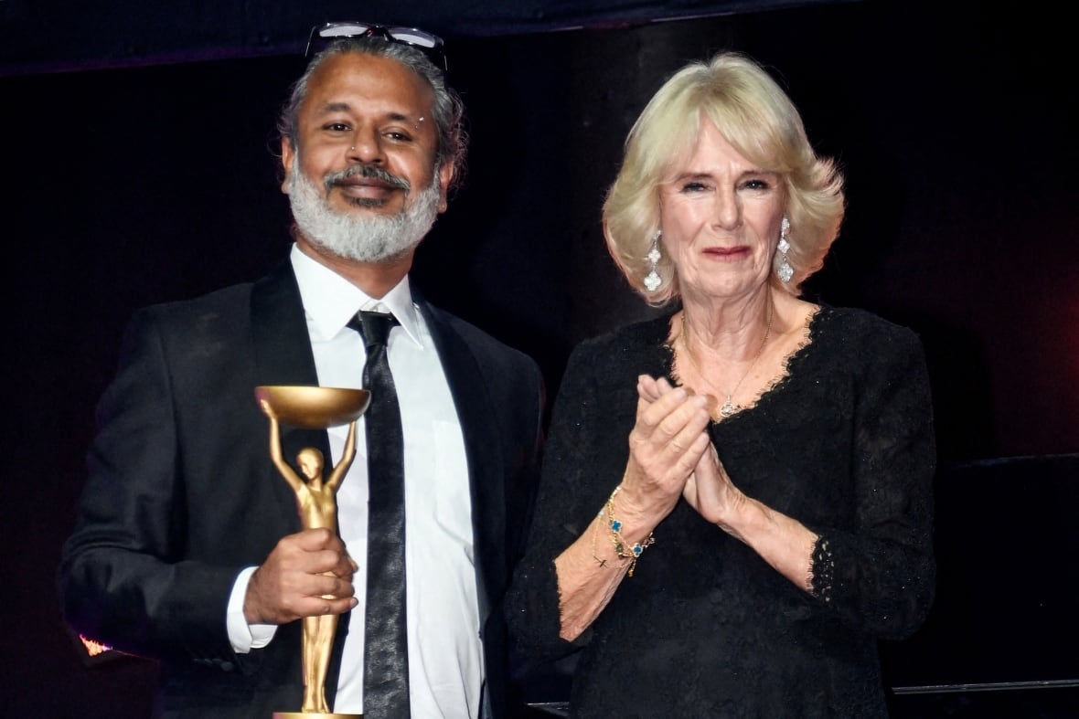 A person holding a trophy stands next to a person clapping.