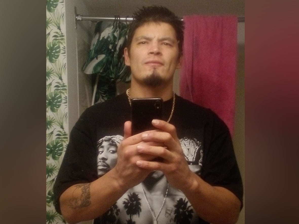 A dark-haired man wearing a black T-shirt poses for a selfie in a mirror.