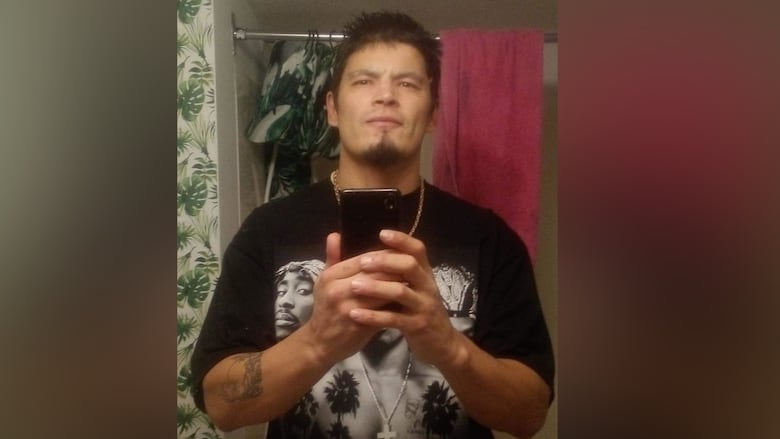A dark-haired man wearing a black T-shirt poses for a selfie in a mirror.