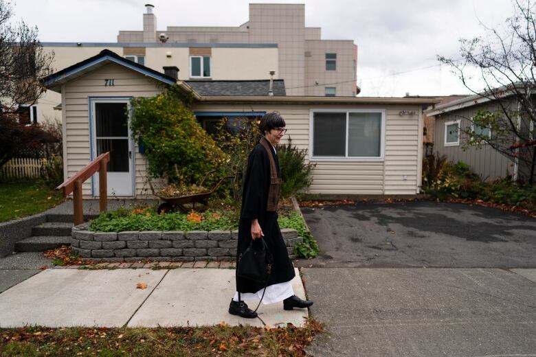 A woman walks down the street dressed in long garbs.