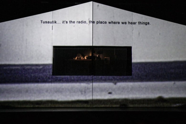 A projection is cast on a structure in the shape of the house. At the top is a sentence "Tusautik... it's the radio, the place where we hear things."