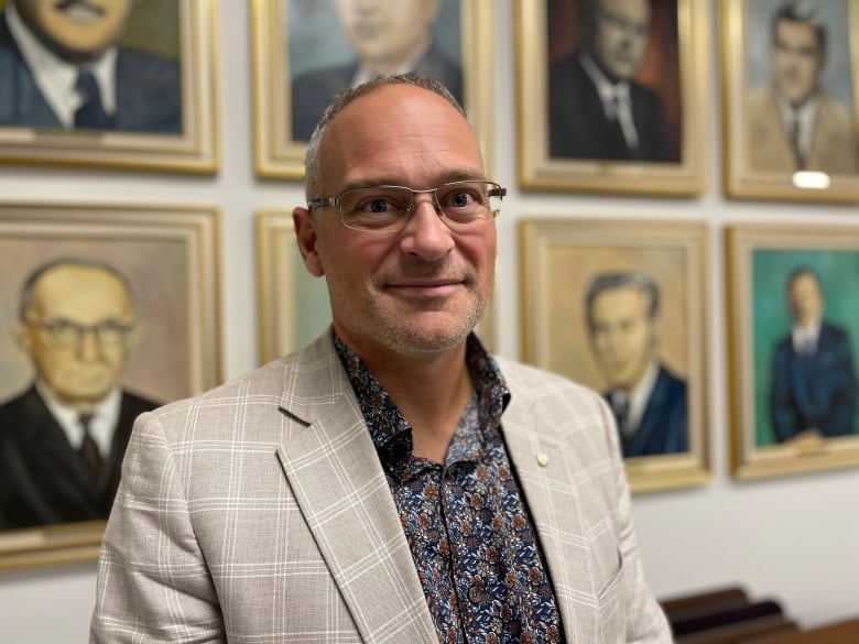 A man with glasses in a pinstriped suit and floral shirt is looking straight into the camera. Portrait of the former mayor of Ke Amos. I see behind him.