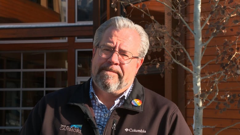 A man wearing a Town of Canmore jacket looks into the distance.