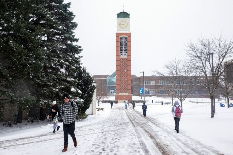 People walking on a snow-covered college campus. There is a large clock tower in the background. 