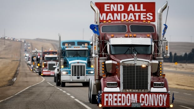 Anti-COVID-19 vaccine mandate demonstrators leave in a truck convoy after blocking the highway at the busy U.S. border crossing in Coutts, Alta., Tuesday, Feb. 15, 2022.THE CANADIAN PRESS/Jeff McIntosh A line of semis can be seen on the highway, driving away from the protest. On top of the first truck sits a red and white sign reading "end all mandates."