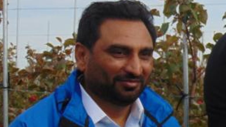Kamalpreet Khaira is pictured standing in front of then agriculture minister Alan McIsaac at a Canadian Nectar Products event. McIsaac is picking a red apple from the tree.