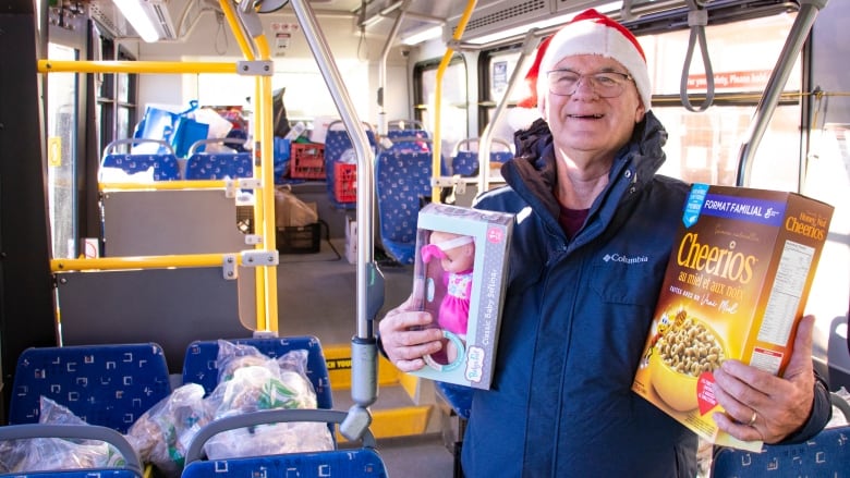 A man wearing a Santa hat smiles while holding donations for food hampers and kids toys.