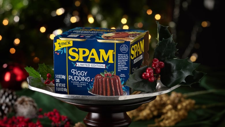 A case of Spam on a silver bowl, surrounded by holly, in front of a Christmas tree. The dark blue box has a picture of Spam molded into the shape of a fruit cake. It reads: SPAM, Limited Edition, Figgy Pudding." A smaller font below reads: "Flavor, Spice & Everything Nice.'