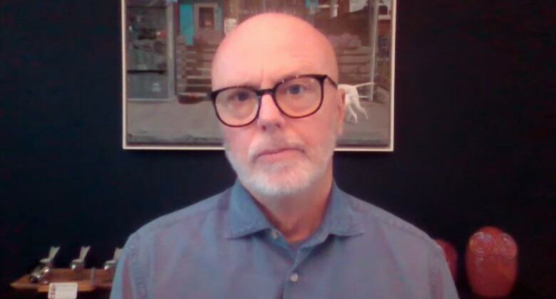 Dr. Michael Gardam stands in front of a painting and looks into a camera.