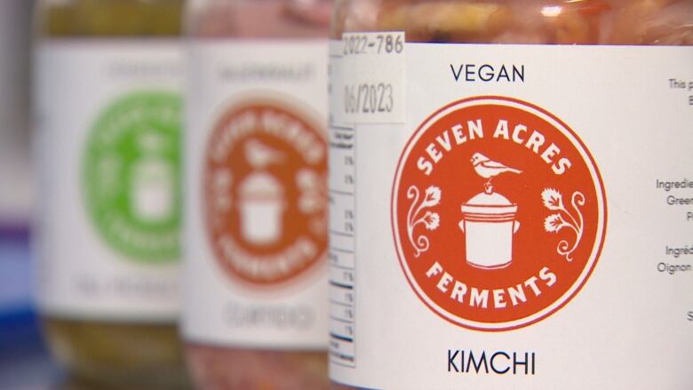 Three jars labelled with the name "Seven Acres Farm" are in a line. The first jar holds Kimchi, and is in focus while the other jars are out of focus.