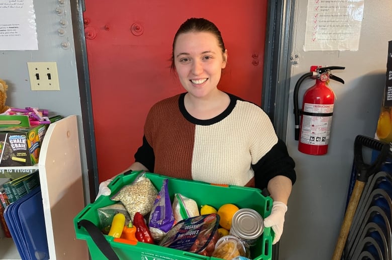 A woman holds a green box full of vegetables 