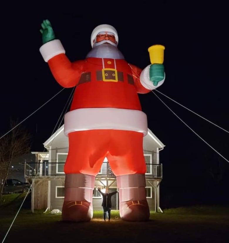 A person stands underneath a tower-sized Santa Claus.