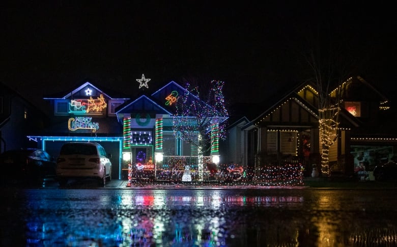 A Christmas lights display at a house on a city street, with the lights reflecting onto the wet street. 