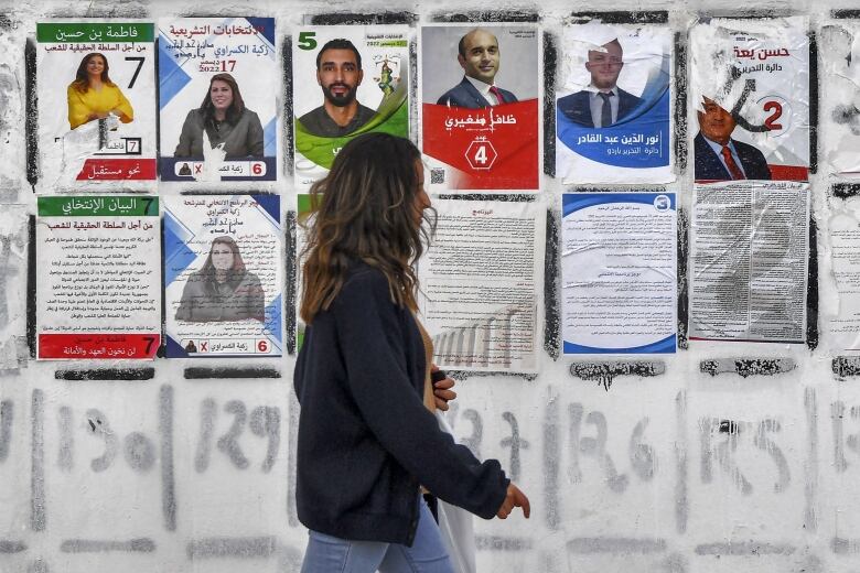 A person walks past electoral posters on a wall displaying candidates running in the Tunisian national election scheduled for Saturday.