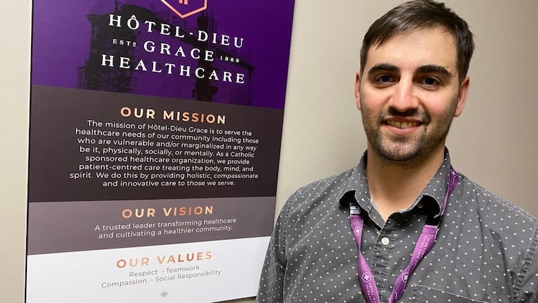 Kevin Matte stands next to a Hotel-Dieu Grace Healthcare sign, mounted to a wall, that explains the organization's mission, vision and values.