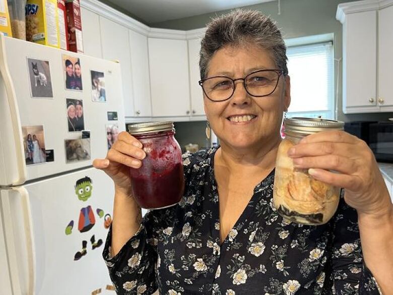 woman in kitchen, smiling, holding up jars of food