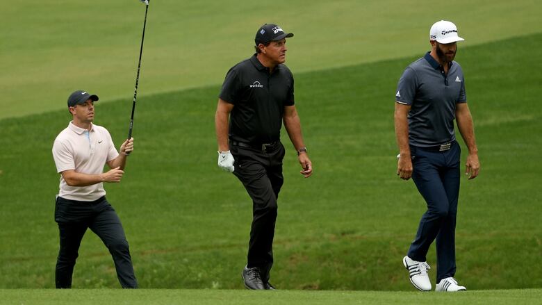 Three golfers walk one by one on grass as the latter hold a club in the air.