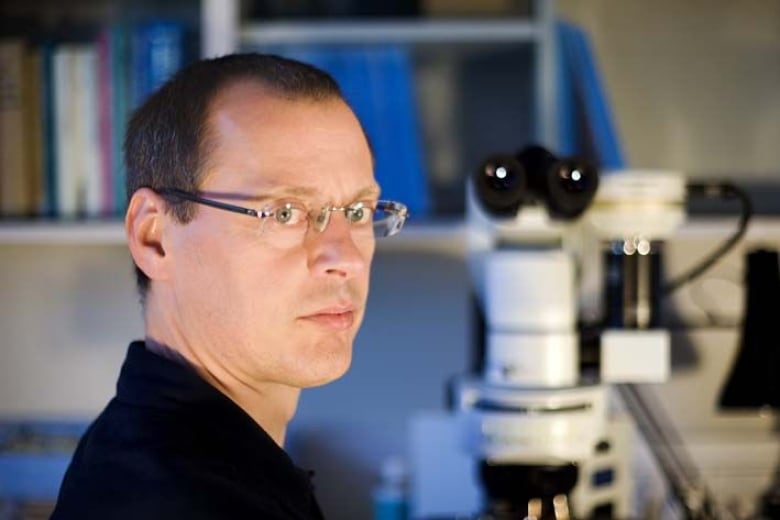 A man with glasses next to a microscope. 