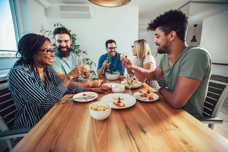 A diverse group of people are pictured at a table, raising champagne glasses, enjoying a meal.