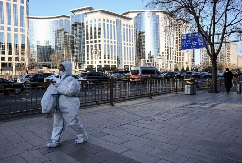 A woman wearing personal protective equipment walks on the street in Beijing.